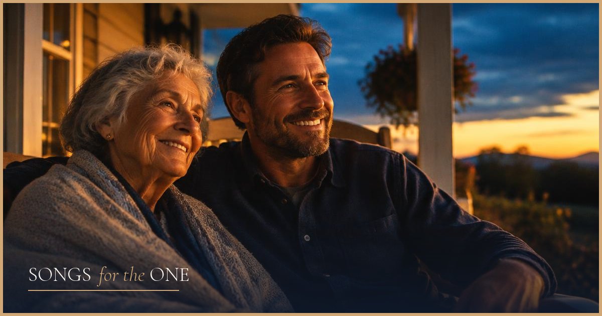 A smiling elderly mother and her adult son sitting together on a porch at sunset